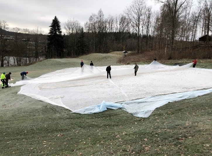 9 people spreading a cover on turf at a golf course in the fall