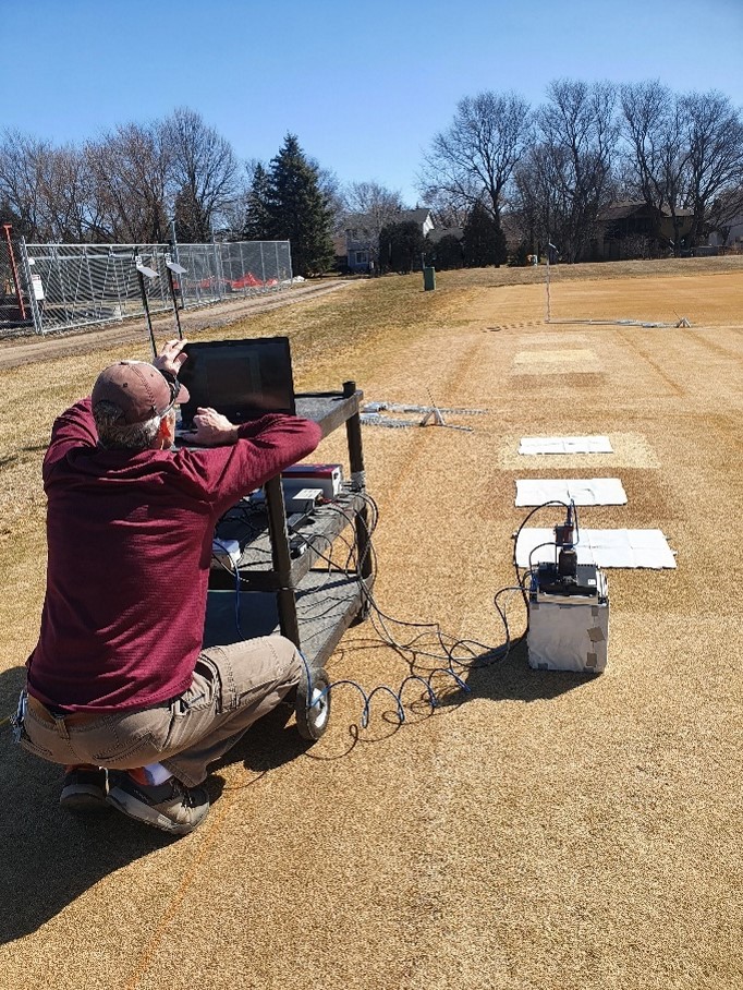 A person looking at a laptop computer on a stand outside on turfgrass research plots